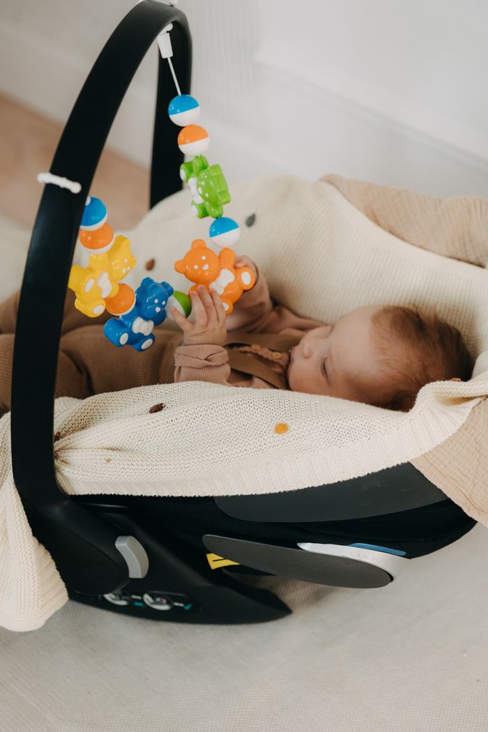 Home Infant in a cozy car seat playing with hanging colorful toys indoors.