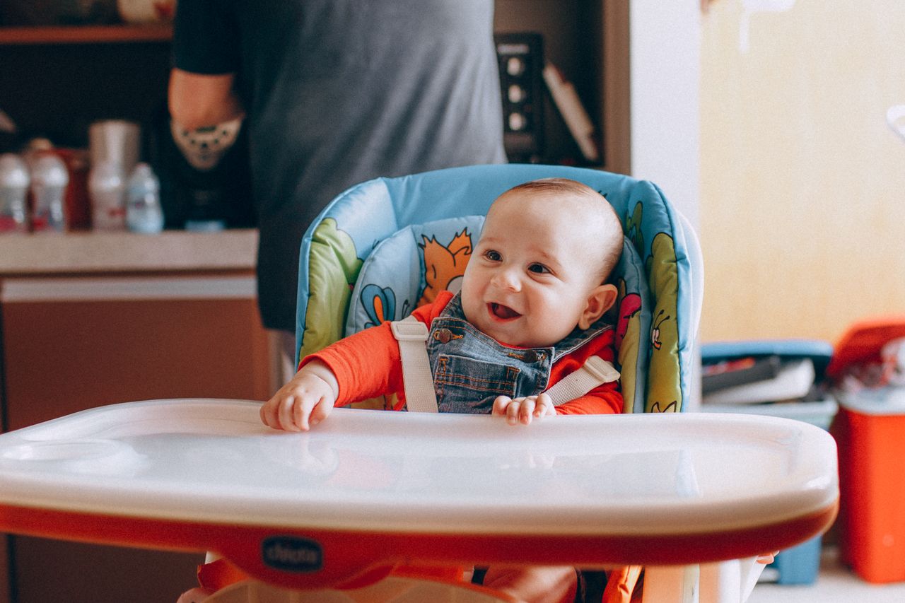 Home Adorable little baby in chair smiling brightly while waiting for food in kitchen