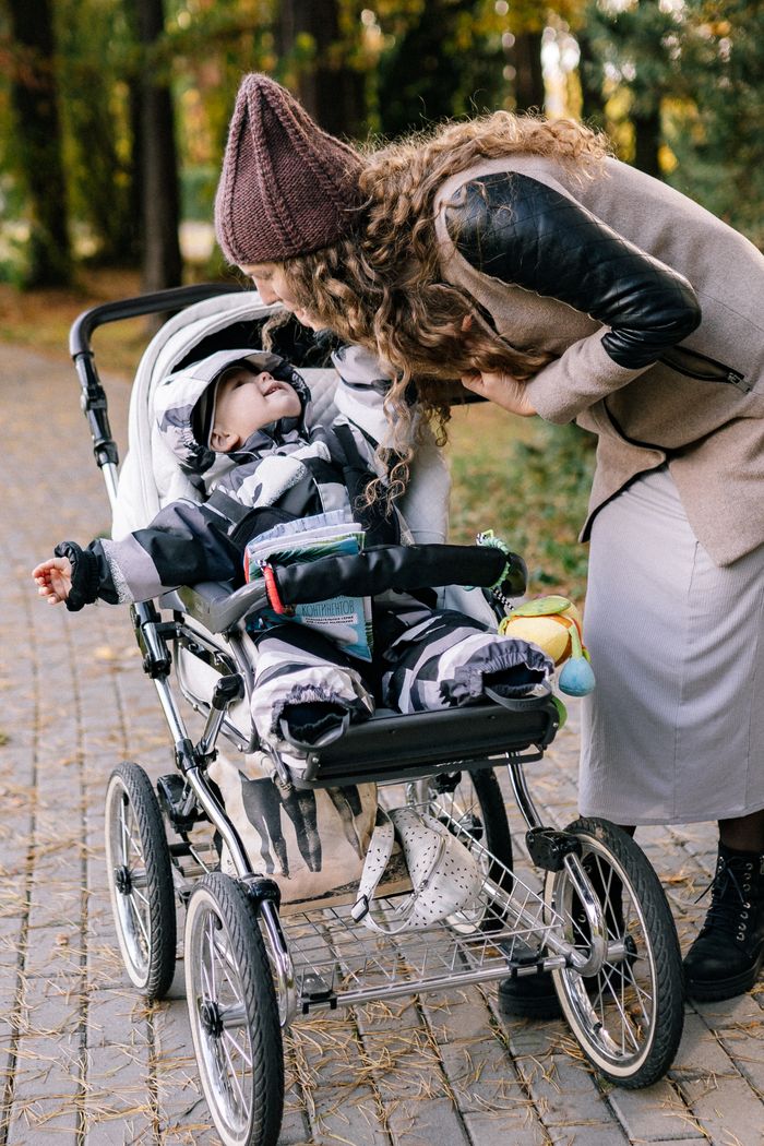 Home A mother bends over a stroller in a park during autumn, enjoying quality time with her baby.