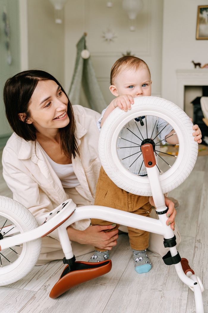 Services Happy mother and toddler enjoying time with a bicycle indoors, showcasing love and playfulness.